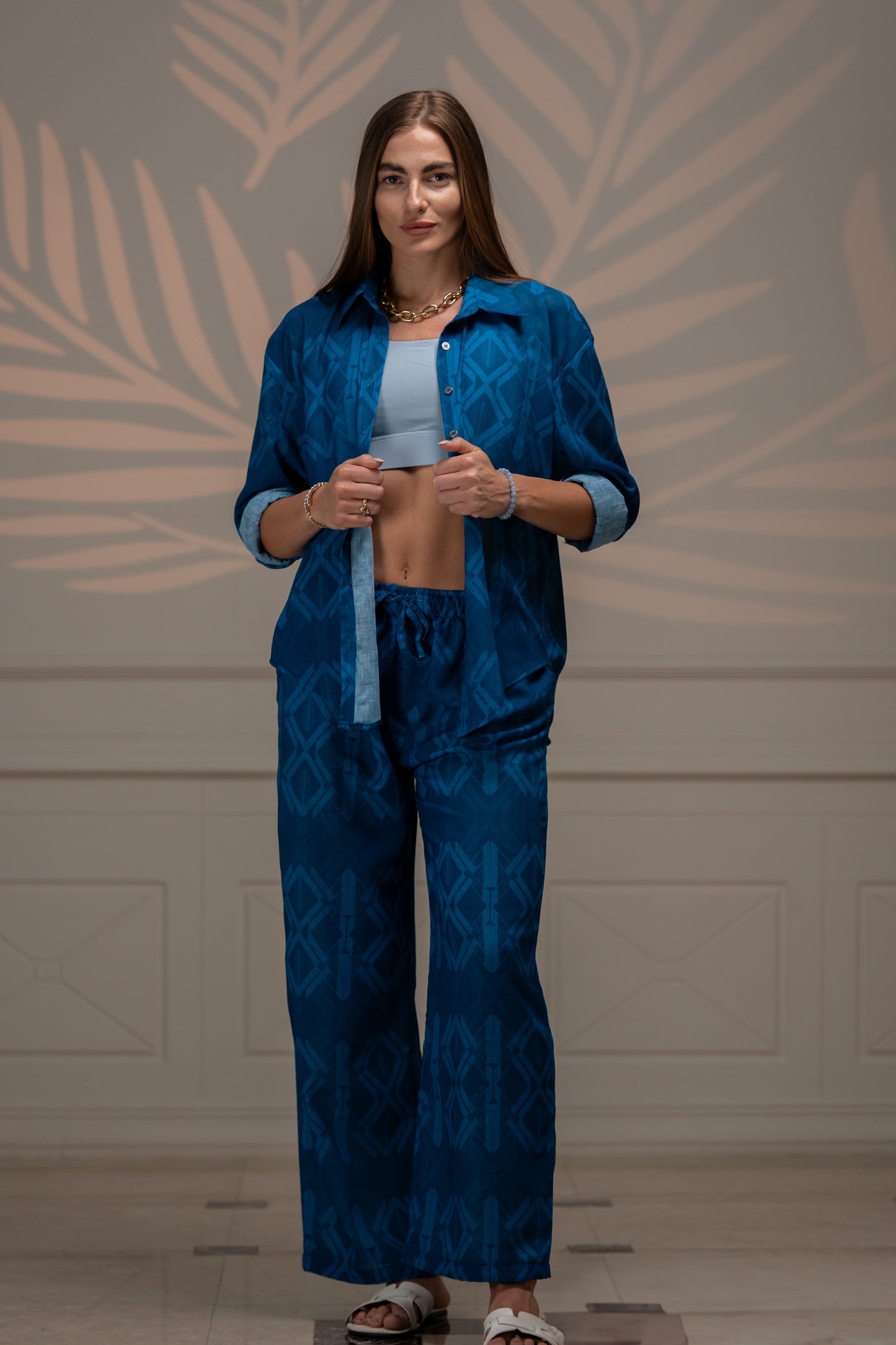A relaxed-fit linen Sunline Shirt in blue with a classic button-front design, long sleeves, and a curved hem. The lightweight, breathable fabric has subtle texture, perfect for casual or beachwear. Styled untucked over white shorts for a laid-back summer look.