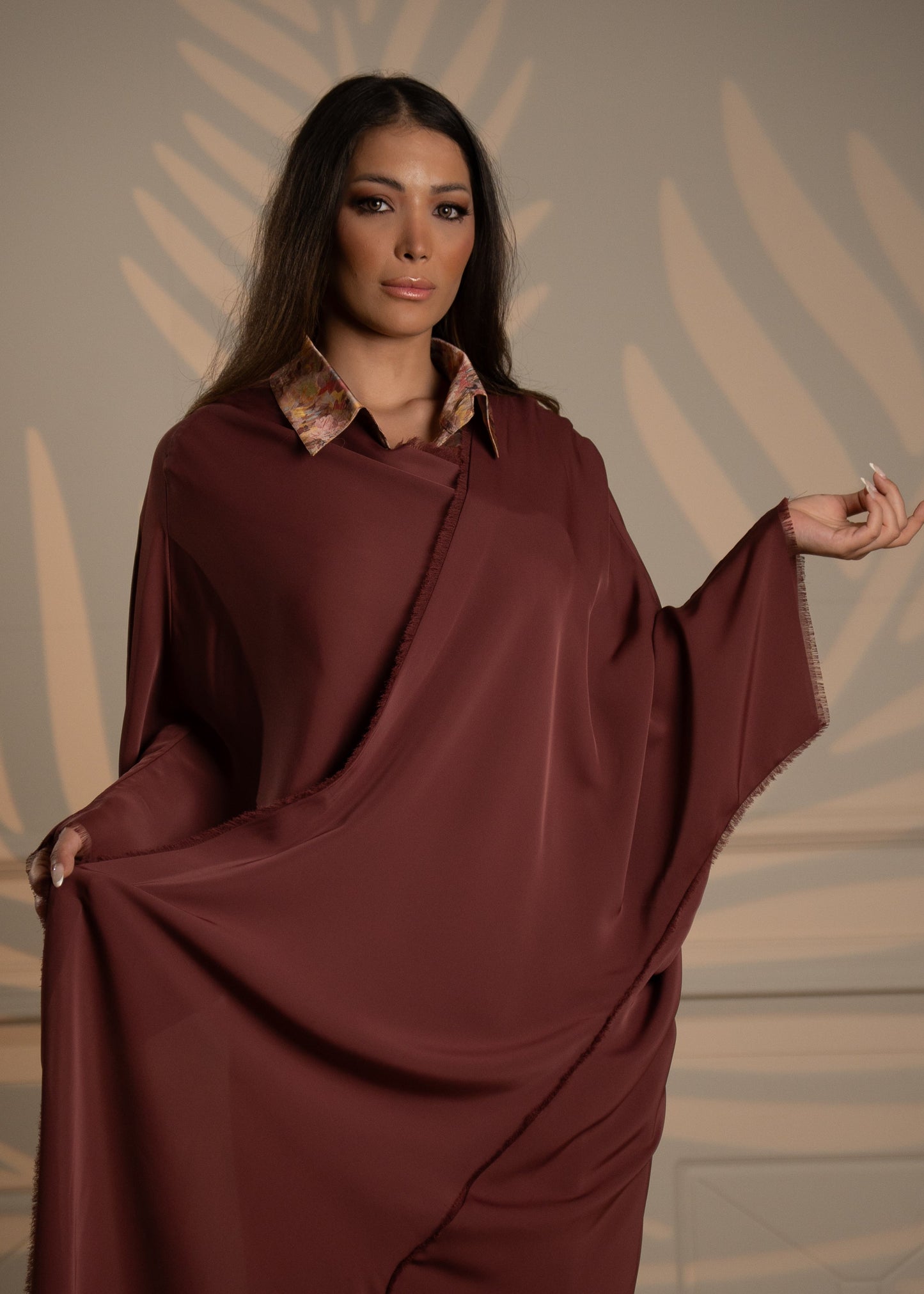 Woman wearing a burgundy dress with a patterned collar against a decorative wall.