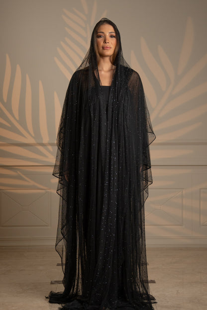 Woman wearing a black dress with a sheer overlay against a neutral background