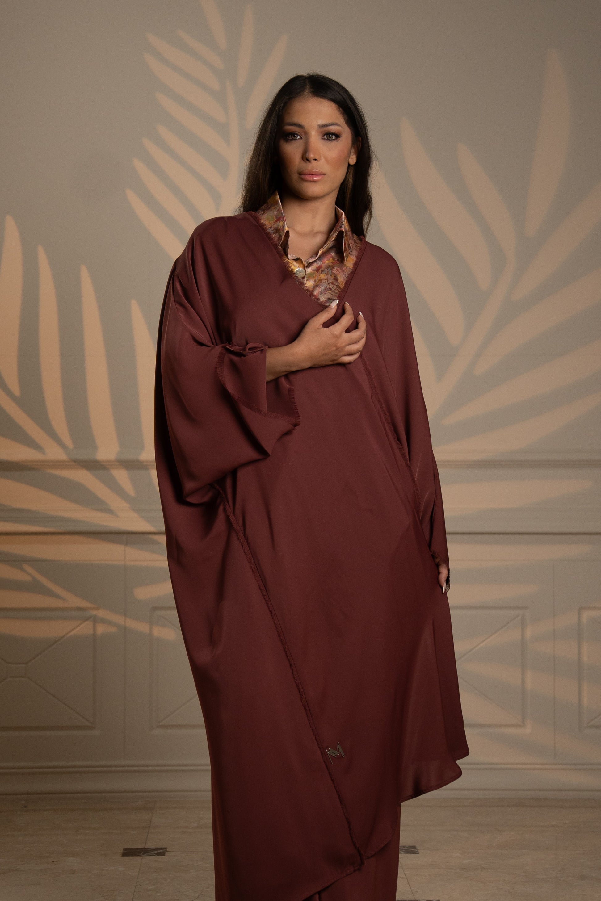 Woman wearing a burgundy dress against a decorative wall.